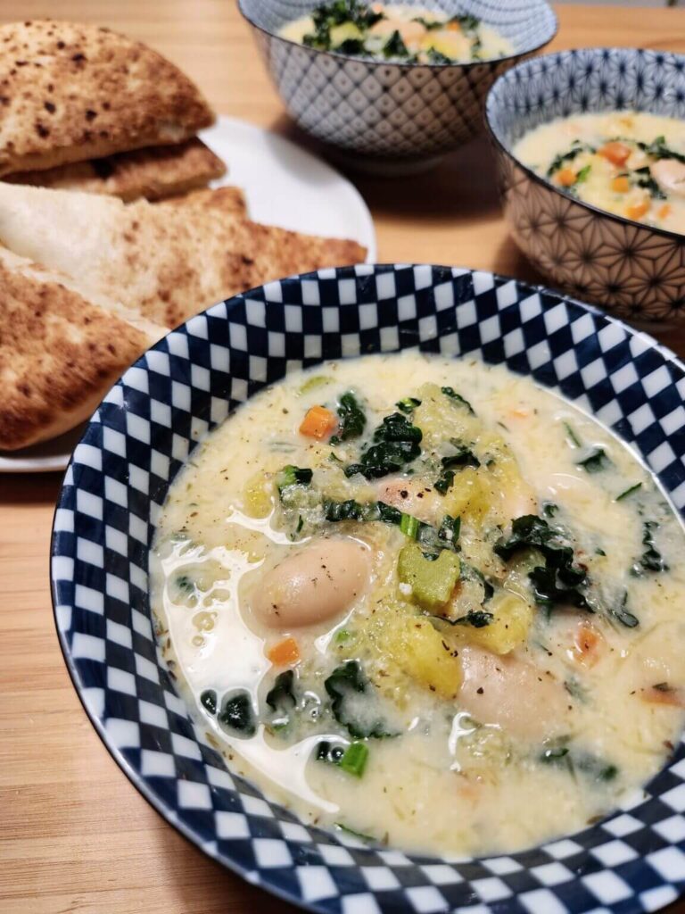 A bowl of soup with bread in the background